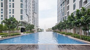Ein Schwimmbecken mit Holzterrasse im Vordergrund, gesäumt von hohen Wohngebäuden mit Balkonen und Grünpflanzen.