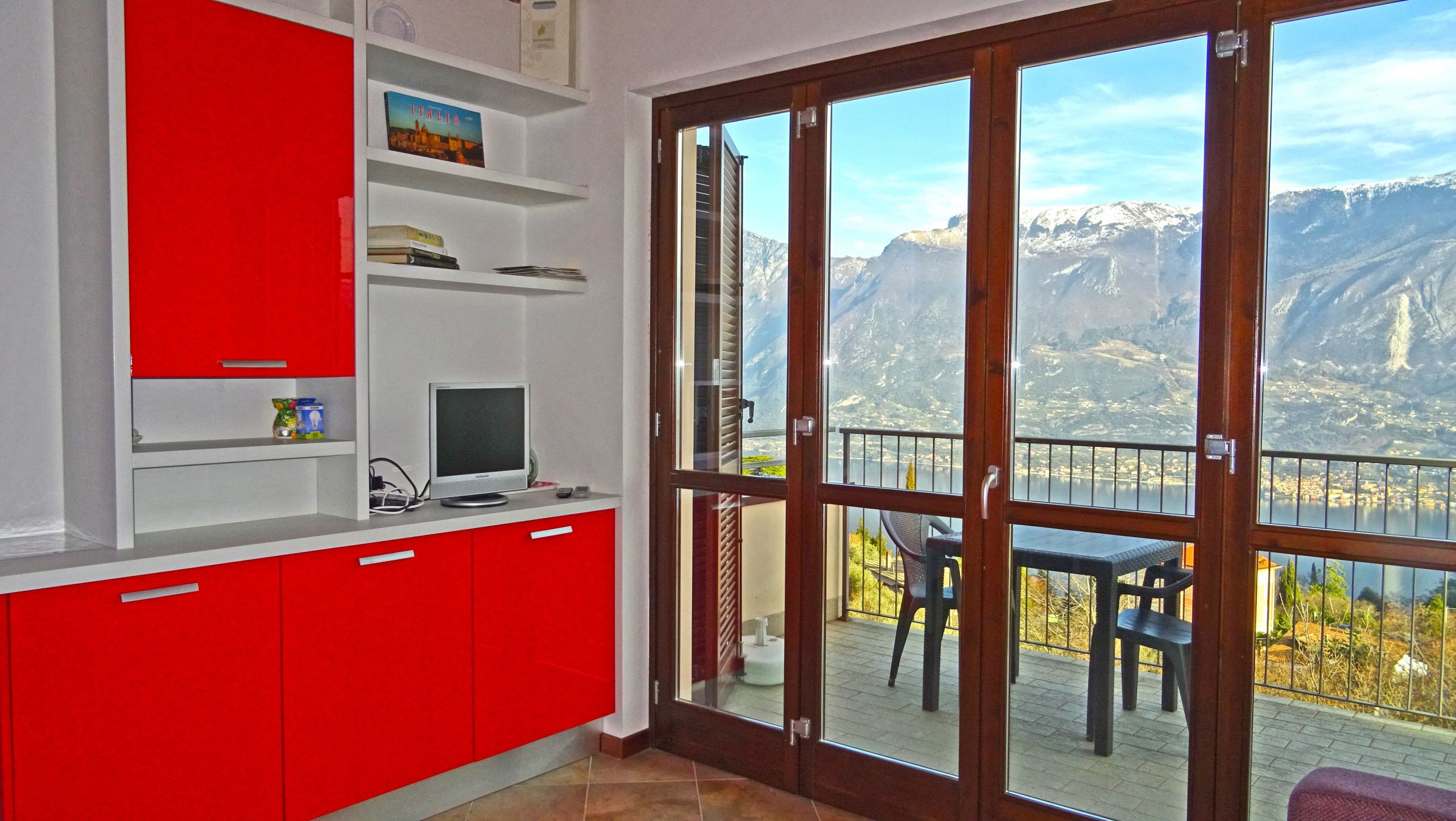 A room with a red cabinet, a television, and a large sliding glass door leading to a balcony with a mountain view.