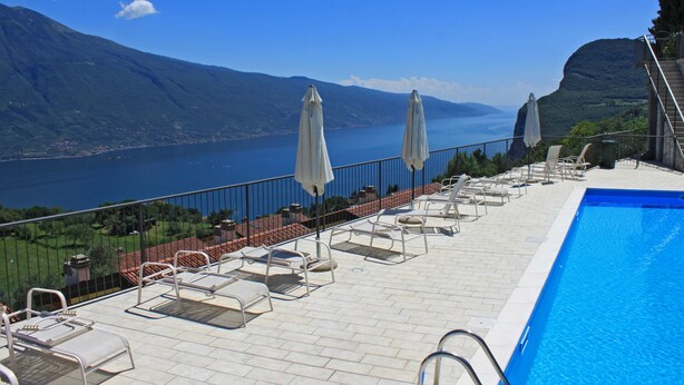 A poolside area with lounge chairs and umbrellas overlooking a lake and mountains. - La Quiete 56 Holideal (Tremosine)