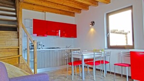 A modern kitchen with red cabinets, a dining area with white chairs, and a large window providing natural light. - La Quiete 56 Holideal (Tremosine)