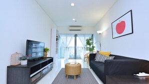 A modern living room with a black sofa, a television on a black stand, a wicker ottoman, and a framed picture on the wall. - S1 Awesome 1BR near KLCC - KL Tower - Hi Speed WIFI (Kuala Lumpur)