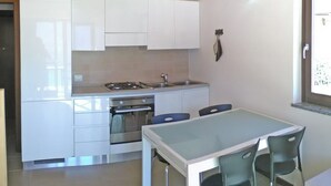 A compact kitchen with white cabinets, a gas stove, and an oven. There is a dining table with two chairs. - La Quiete 58 Holideal (Tremosine)