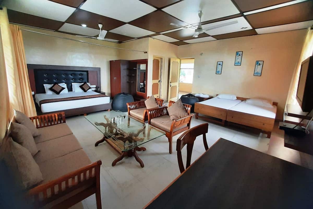 Habitación de hotel con cama, sofá, mesa de comedor, sillas, mesa de centro de vidrio y ventilador de techo.