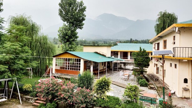 A residential area with a house featuring a green roof, a balcony, and a garden with pink flowers.