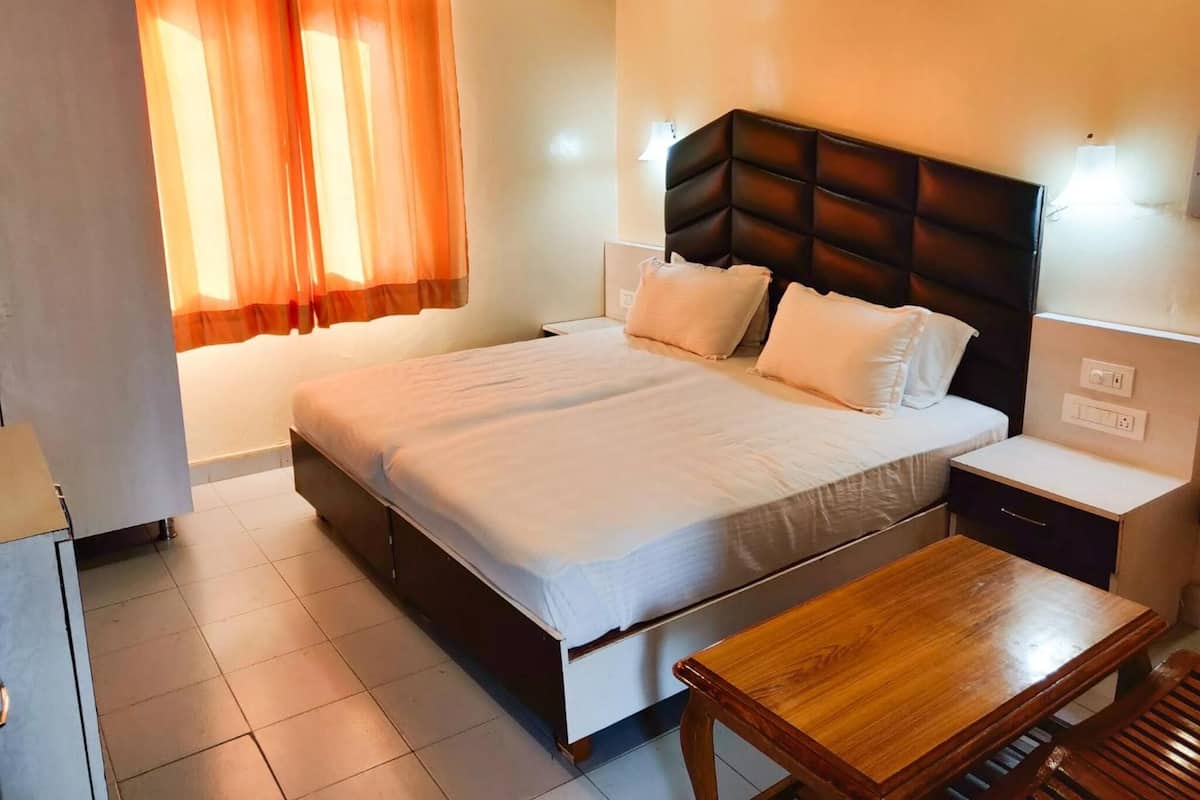 Habitación de hotel con una cama grande, mesitas de noche, un escritorio de madera y una ventana con cortinas.