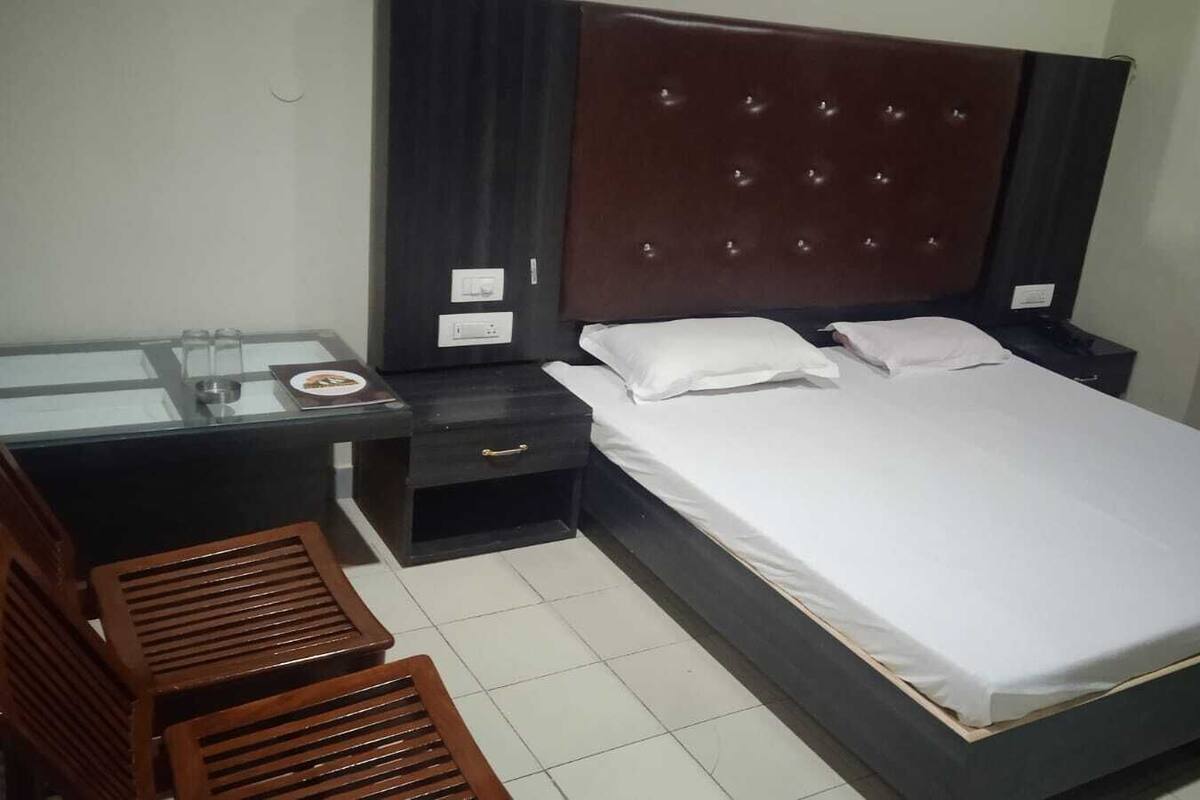 Una habitación de hotel con una cama, un escritorio con una silla, una mesita de noche y una pequeña mesa con vasos.