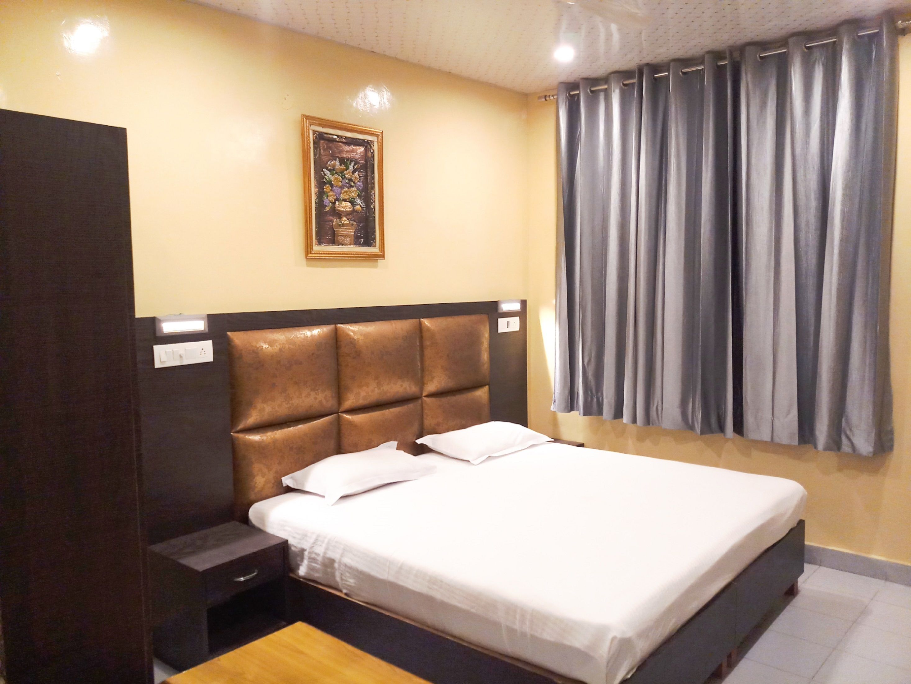 Ein Hotelzimmer mit einem Bett, einem Nachttisch, einer Holzbank, einer Wandleuchte und einem gerahmten Bild.