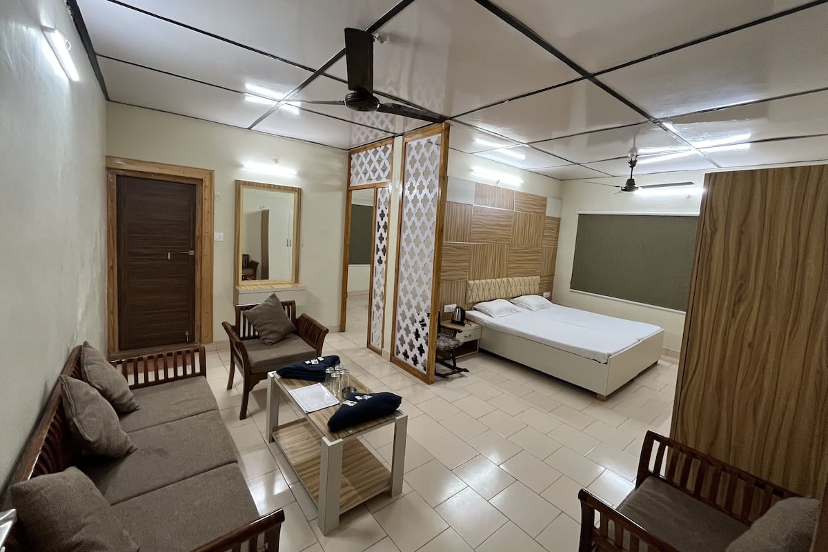 Una habitación con una cama, dos sofás, una mesita, un espejo y una separación.