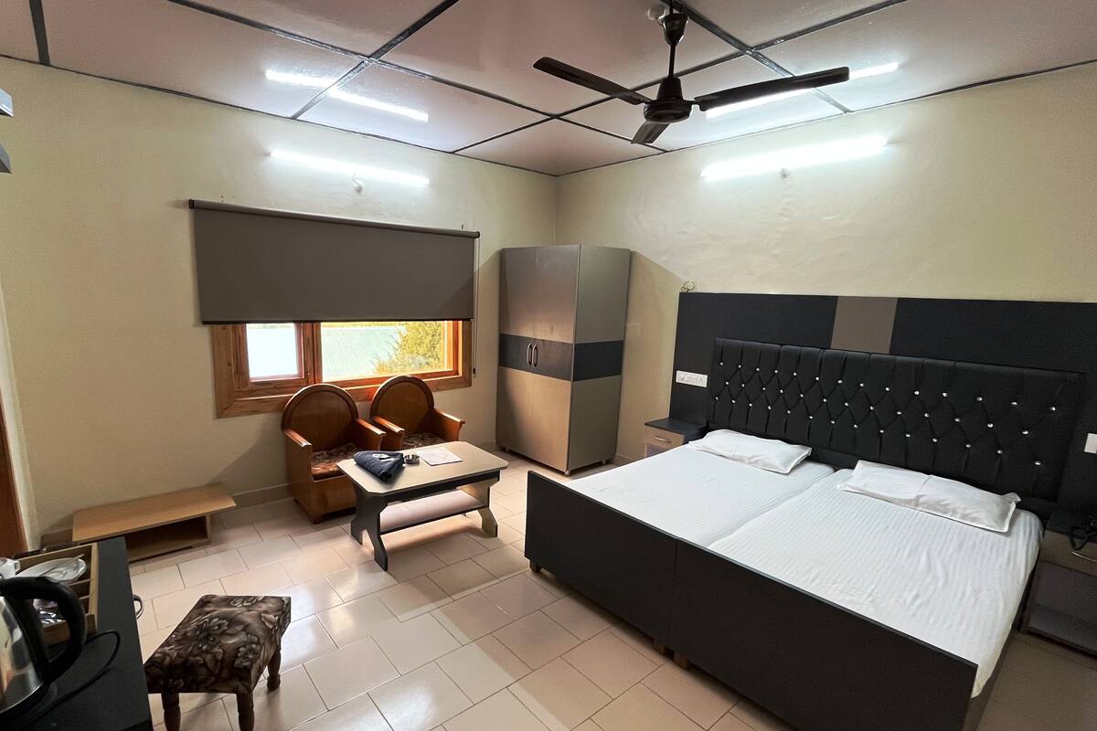 Habitación de hotel con cama, escritorio con sillas, armario, ventilador de techo y ventana.