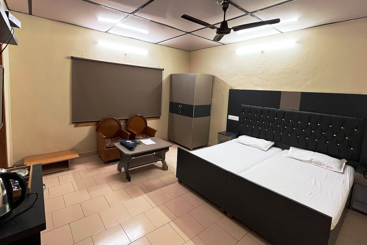 Habitación de hotel con cama, escritorio, silla, armario, televisor y ventilador de techo.