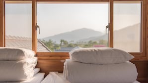 A room with two beds, each with neatly folded white linens, and a large window offering a view of a mountain and a traditional building. - XinFu Traveler Inn (Beinan)