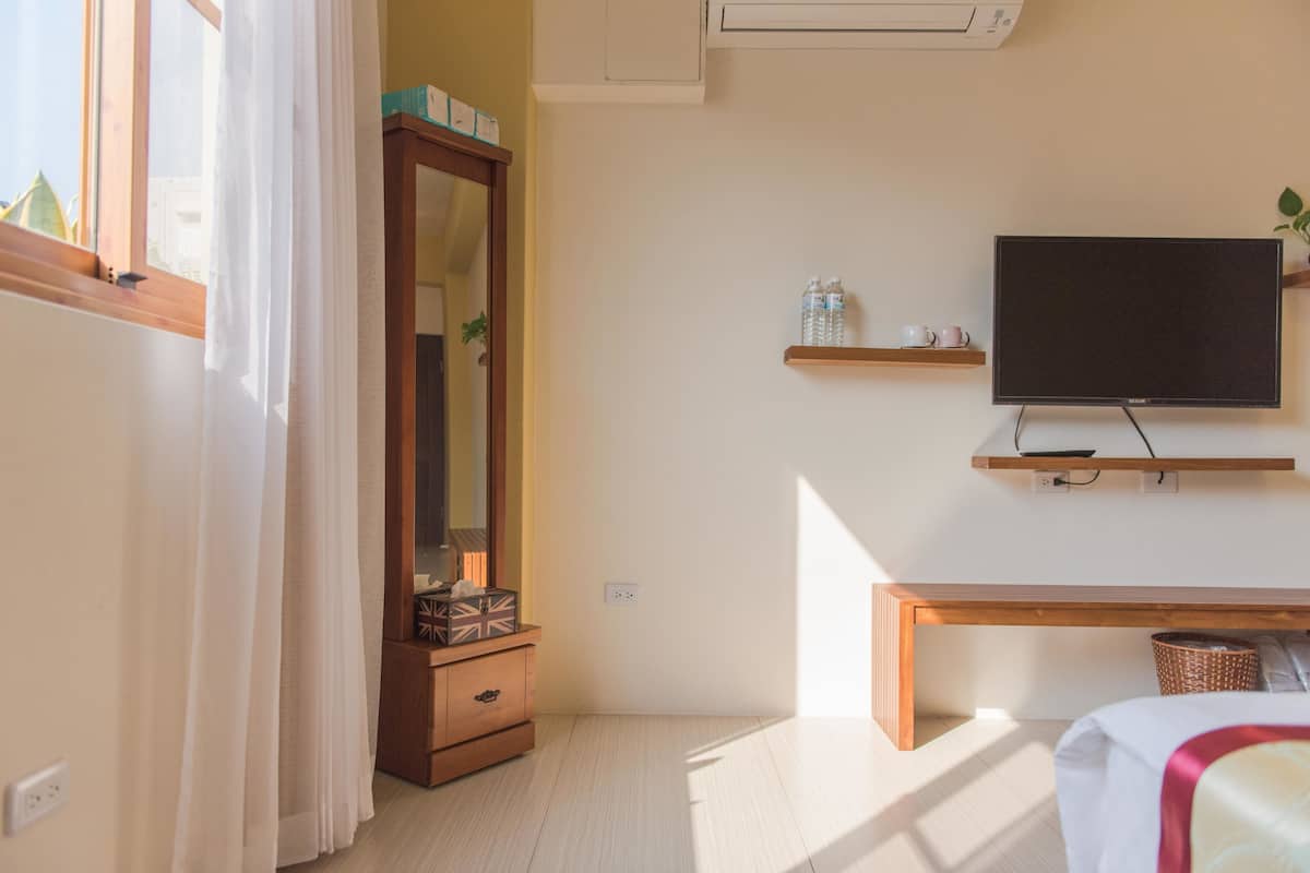 A bedroom with a bed, a TV, a wooden dresser, a mirror, and a shelf with bottles.