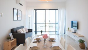 A modern living room with a dining table set for four, a sofa, a TV, and large windows with a view. - A3 FAMILY Suites 4-6pax Jonker Melaka (Malacca City)