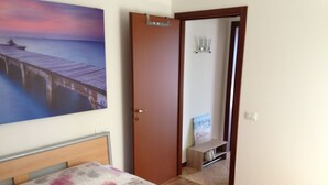 Une chambre à coucher avec un lit, un tableau représentant une jetée, une porte en bois et une petite étagère.