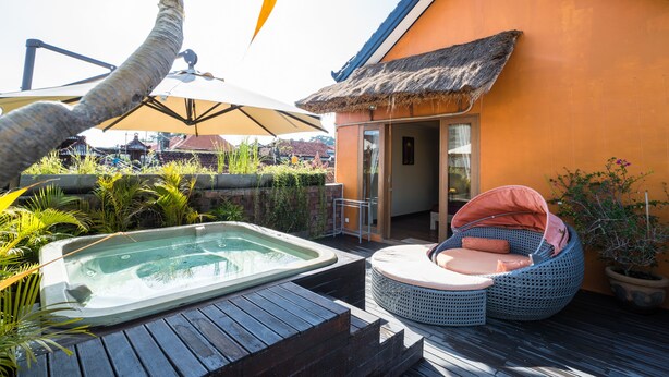 Un jacuzzi, una estructura de techo de paja y una silla lounge de mimbre sobre una terraza de madera.