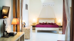 Un dormitorio con una cama de madera, dos mesitas de noche con lámparas, una mesita auxiliar de madera y un televisor sobre un mueble.
