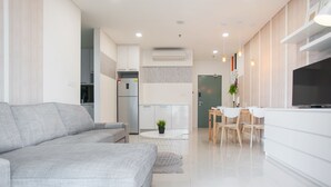 A modern living room with a grey sofa, a dining area with a table and chairs, and a kitchen with white cabinets and a TV. - S6 Beautiful 2 Beds Suite - KLCC - KL Tower - WIFI (Kuala Lumpur)