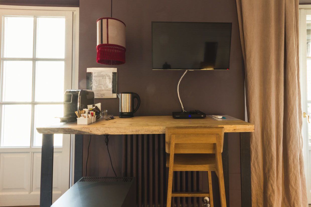 Um espaço de trabalho com uma mesa, um computador, uma luminária e uma TV fixada na parede.