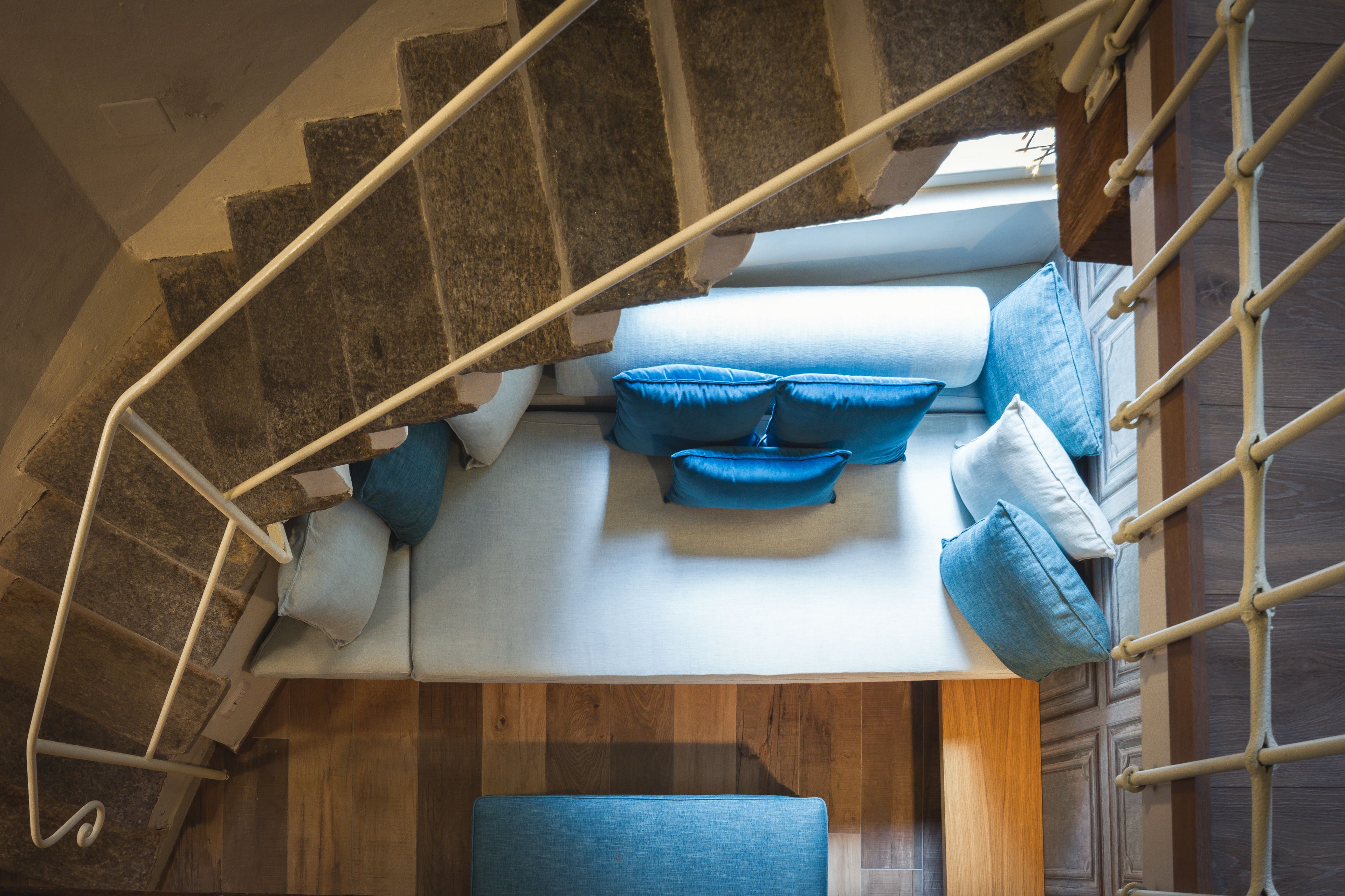 Una escalera con barandilla de madera y una zona de estar acolchada con cojines azules.