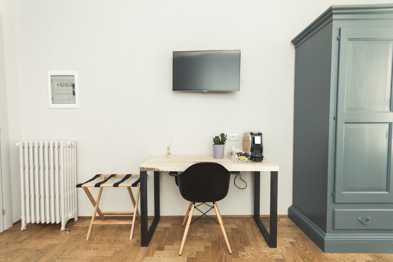 A room with a wooden floor, a white radiator, a small table with a chair, a television mounted on the wall, and a cabinet.
