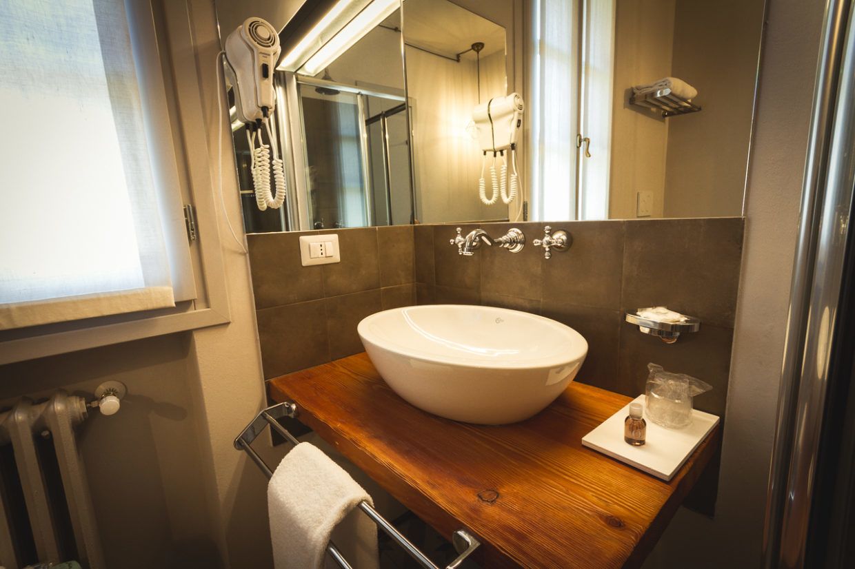A bathroom with a wooden vanity, a large sink, a mirror, a hairdryer, and a towel rack.