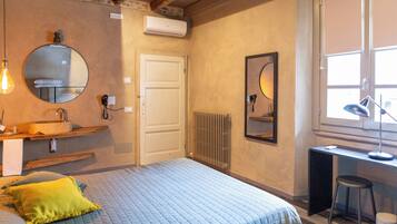 Une chambre à coucher comprenant un lit, une table de chevet, un miroir, un radiateur et une fenêtre. Un bureau et une chaise sont également présents dans la pièce.