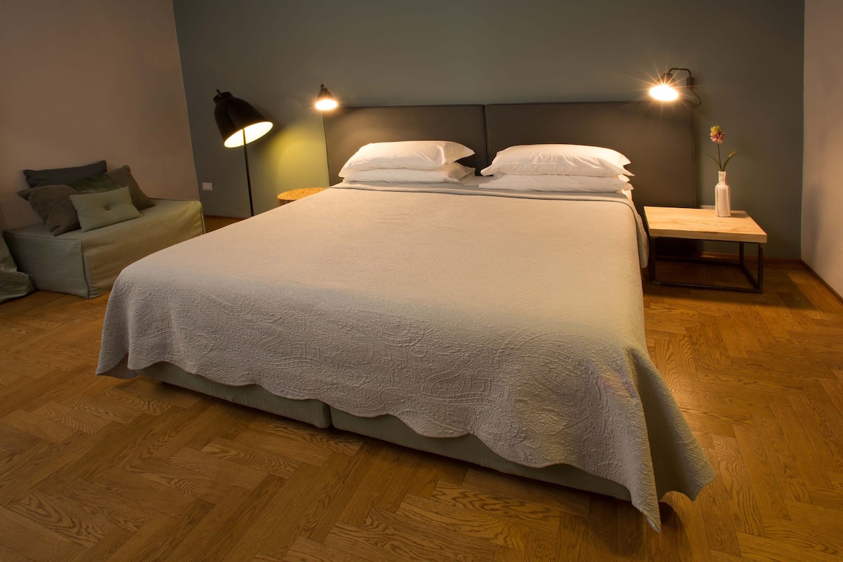 A neatly made bed with a white duvet, a bedside table with a vase, and a floor lamp.