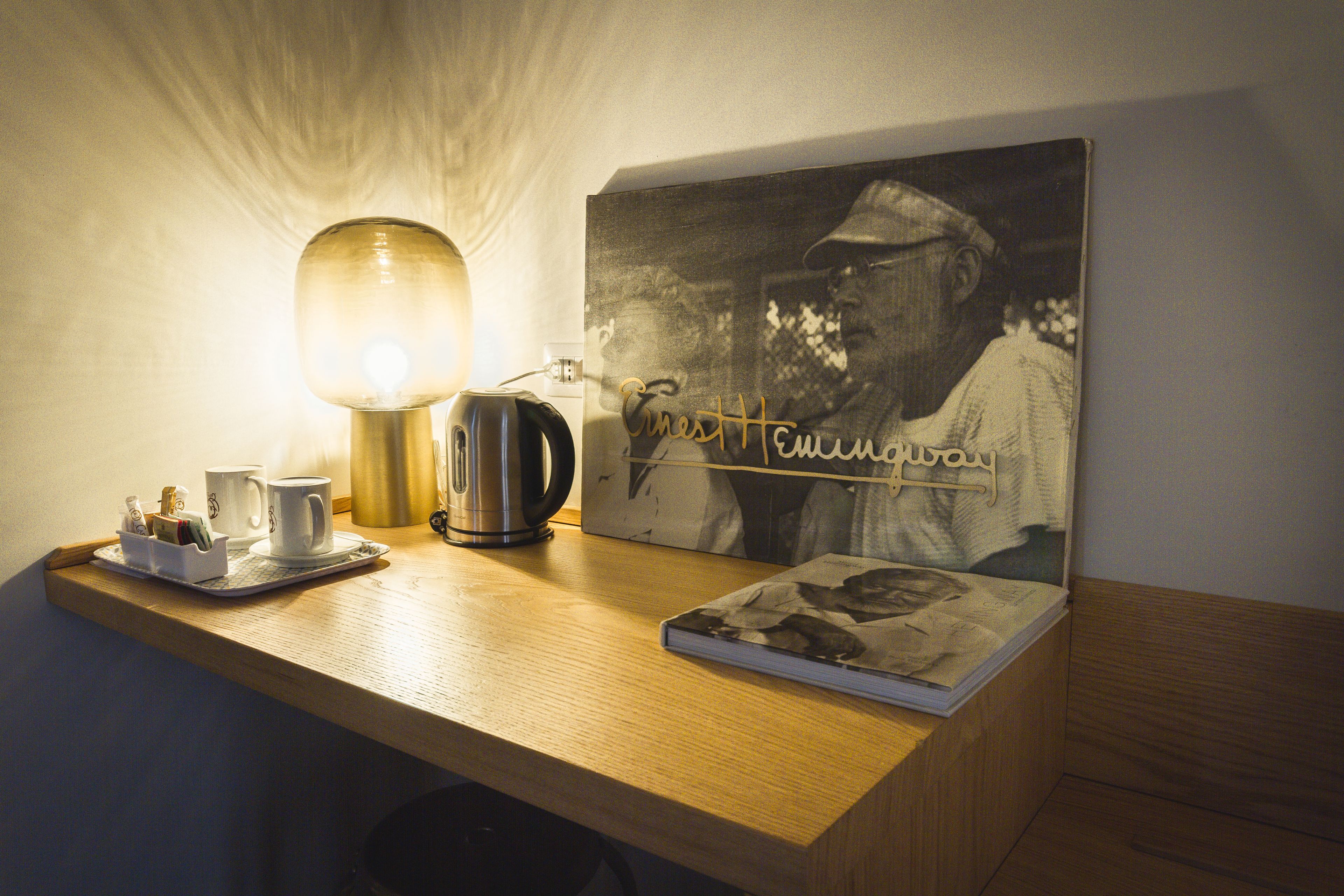 A wooden desk with a lamp, a coffee maker, a tray with mugs, and a framed photograph.