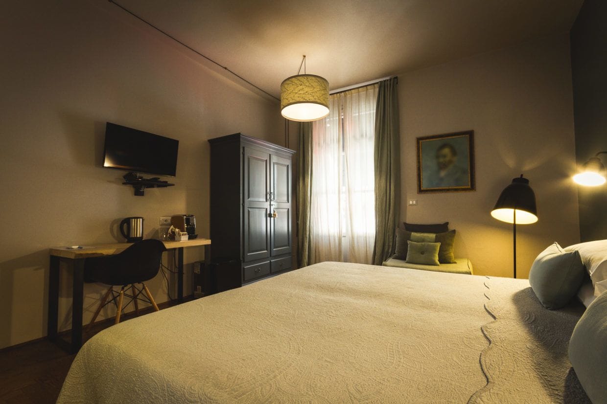 Camera d'hotel con un letto grande, una scrivania con una sedia, una televisione, un armadio, una lampada e un quadro appeso al muro.