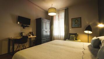 Camera d'hotel con un letto grande, una scrivania con una sedia, una televisione, un armadio, una lampada e un quadro appeso al muro.