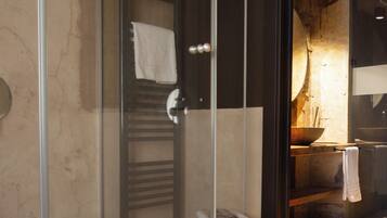 A modern bathroom with a glass shower enclosure, a wooden stool, and a towel rack.