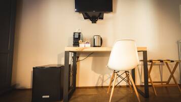 A small, modern room with a wooden desk, a white chair, a black trash bin, and a mounted television.