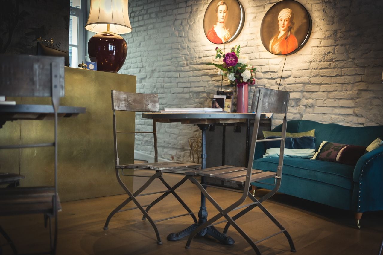 A cozy room with a wooden table, a blue sofa, and a lamp. There are two framed portraits on the wall.