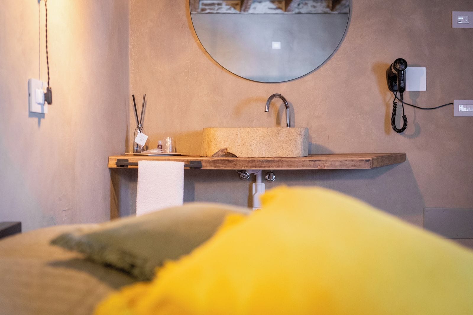 A hotel room with a wooden shelf holding a towel, a round mirror, and a telephone.