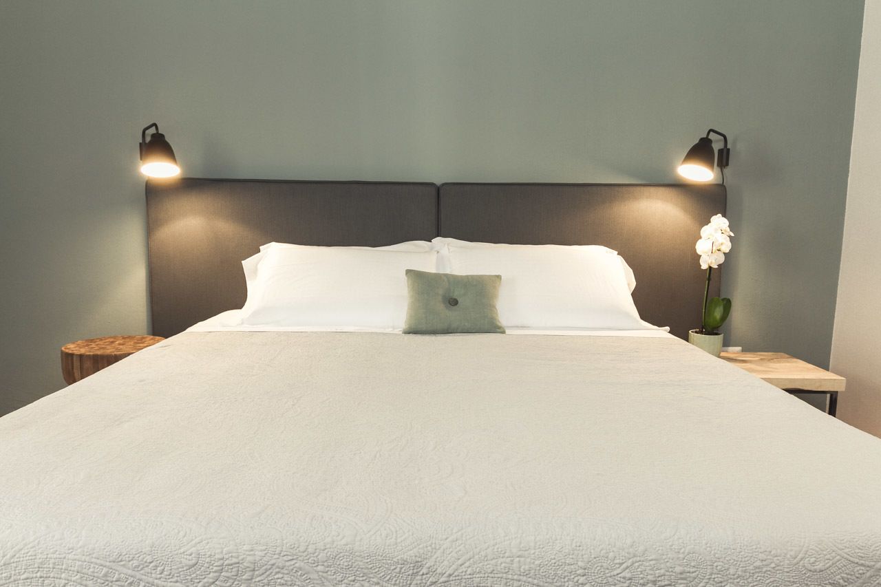 A neatly made bed with white linens, a single green pillow, and two bedside lamps on wooden nightstands.