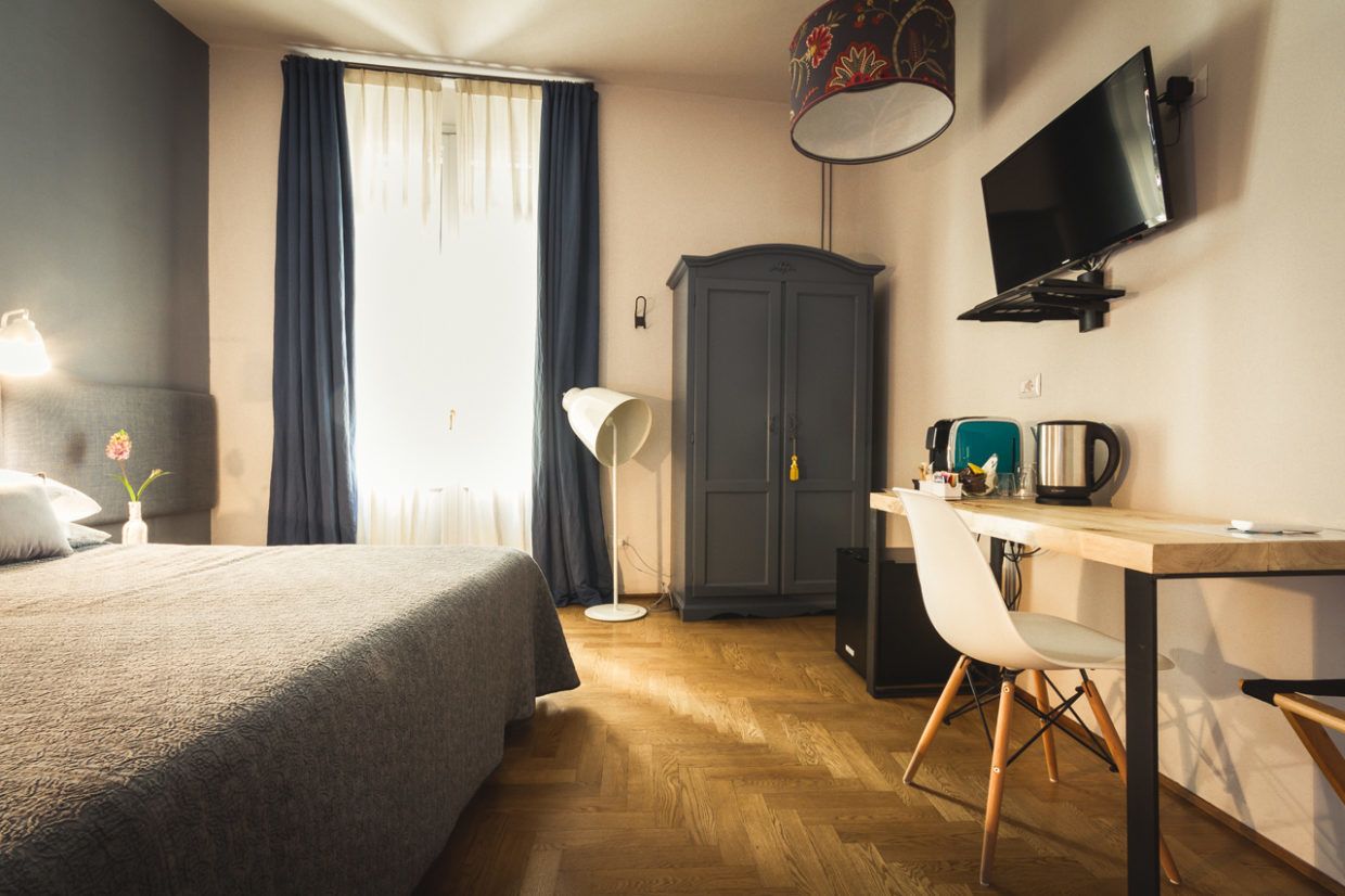 A hotel room with a bed, desk, chair, television, wardrobe, and a window with curtains.