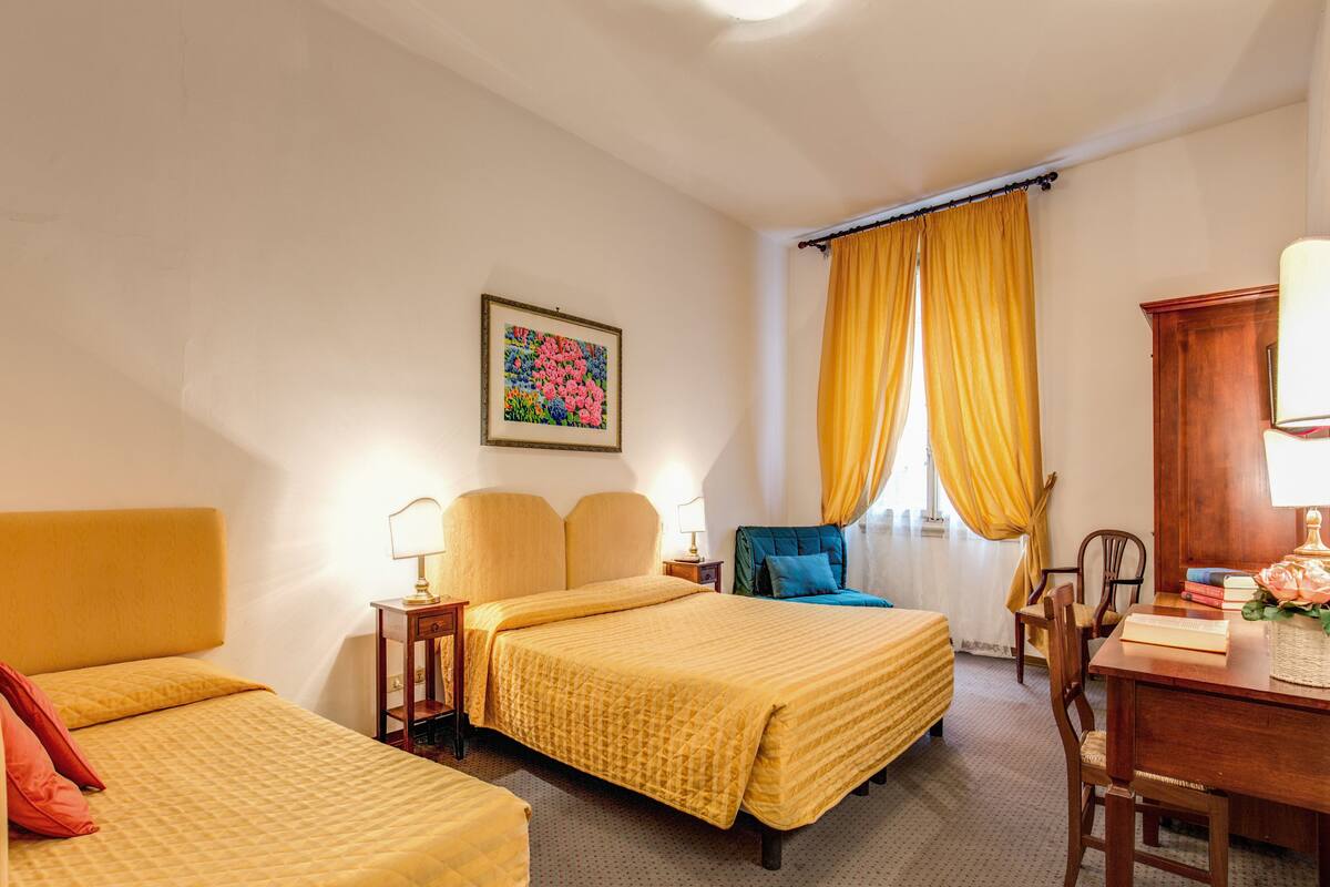 A hotel room with two beds, a desk, a chair, a lamp, and a painting on the wall.