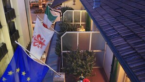 A courtyard with a table and chairs, a flag, and a building with a clock tower in the background. - Hotel San Giorgio & Olimpic Florence (Florence)
