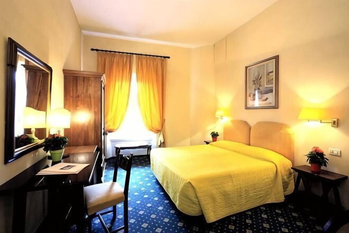 A hotel room with a bed, desk, chair, and a window with curtains.