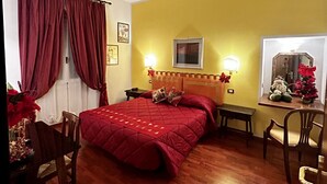 A hotel room with a wooden floor, a bed with a red quilt, a nightstand, a desk, and a chair. - Hotel San Giorgio & Olimpic Florence (Florence)