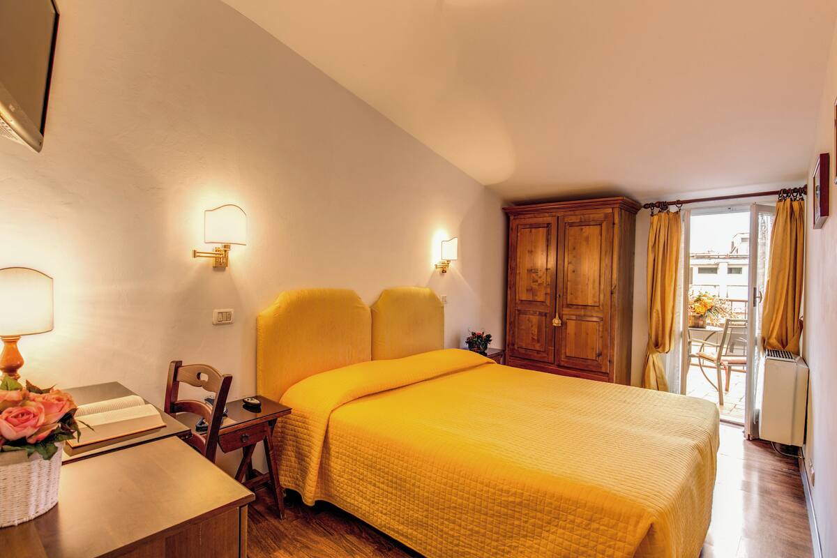 A hotel room with a bed, a desk with a lamp, a chair, and a wardrobe.