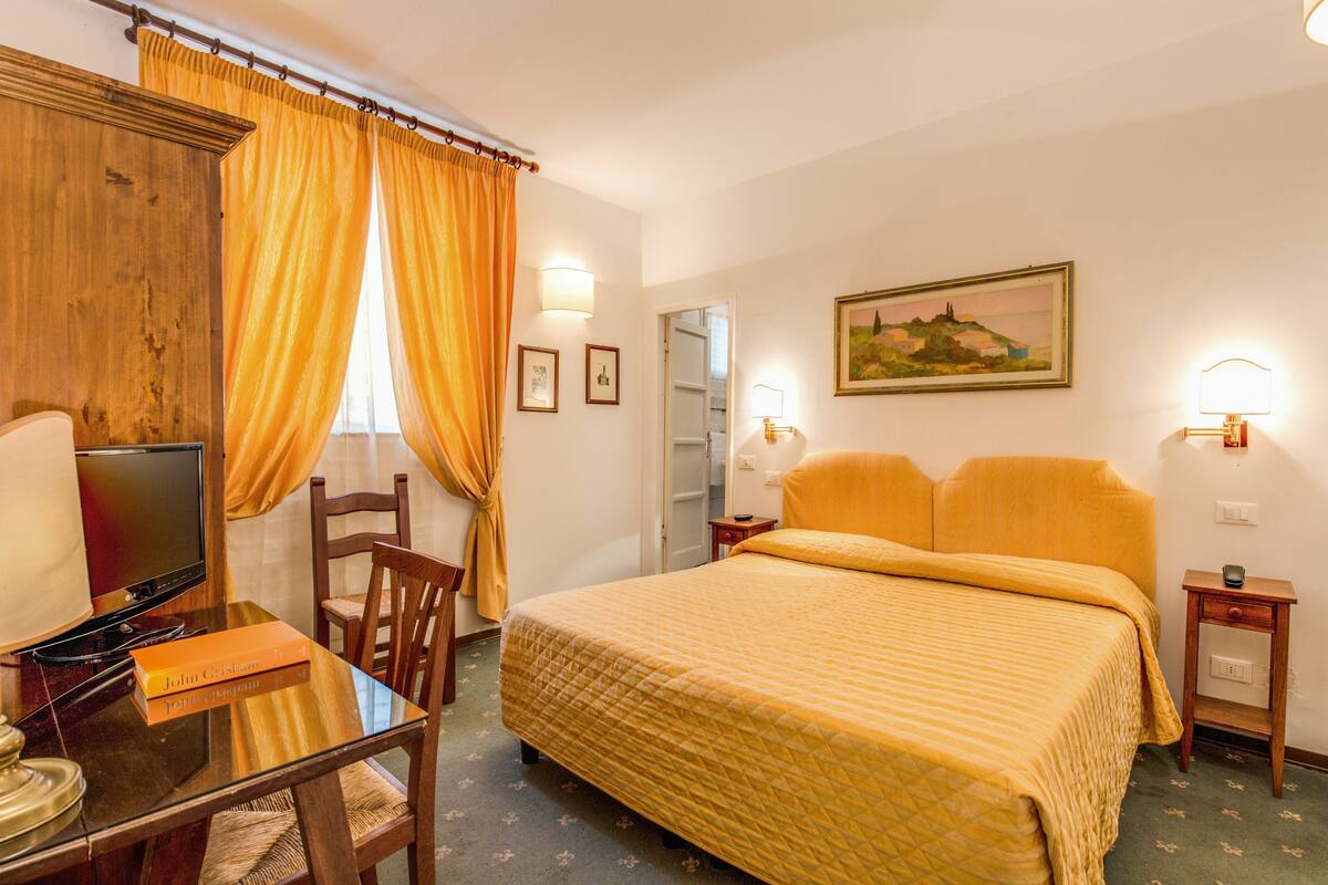 A hotel room with a bed, a desk with a television, and a chair.