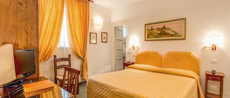 Una habitación de hotel con cama, escritorio con televisor y una silla.