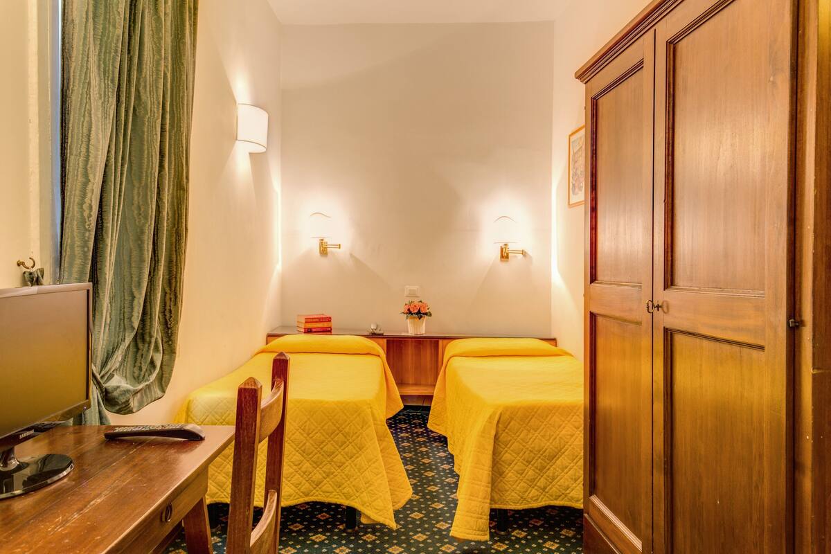 A hotel room with two beds, a desk with a computer, a wardrobe, and a curtain.