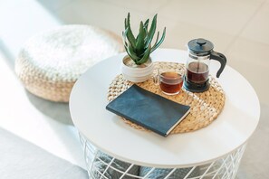 A round white table with a woven placemat, a small potted succulent, a coffee maker, a cup of tea, and a book. - Atlantis Residence by Stayshare Homes (Malacca City)