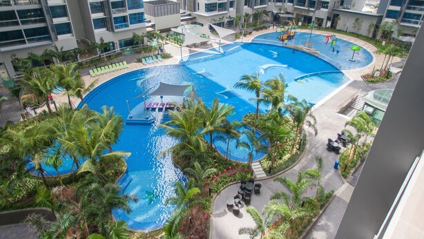 A large indoor swimming pool surrounded by palm trees and lounge chairs, with modern buildings in the background. - Atlantis Residence by Stayshare Homes (Malacca City)