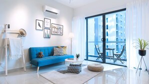 A modern living room with a blue sofa, a round coffee table, and a large sliding glass door leading to an outdoor balcony. - Atlantis Residence by Stayshare Homes (Malacca City)