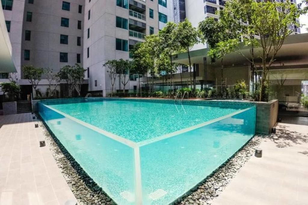A rectangular pool with clear water, surrounded by a pebble border and trees, set in a modern building with multiple floors and balconies.