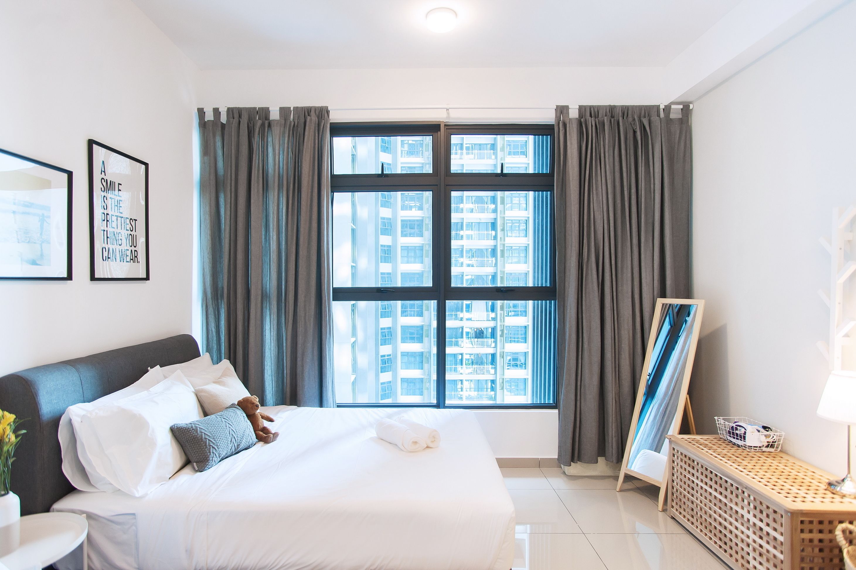 Habitación de hotel con una cama grande, una mesita de noche, una lámpara y vistas de un paisaje urbano por la ventana.