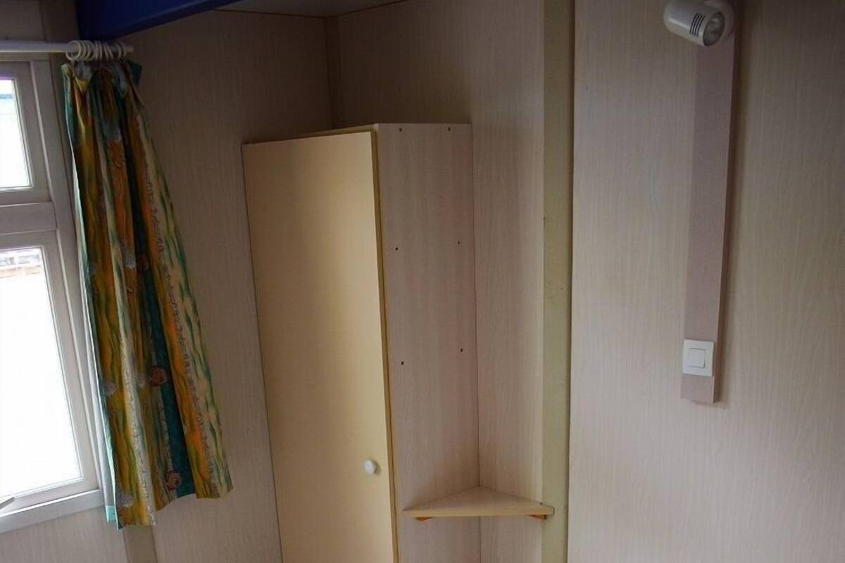 A single bed with white bedding, a wooden wardrobe, and a window with curtains.
